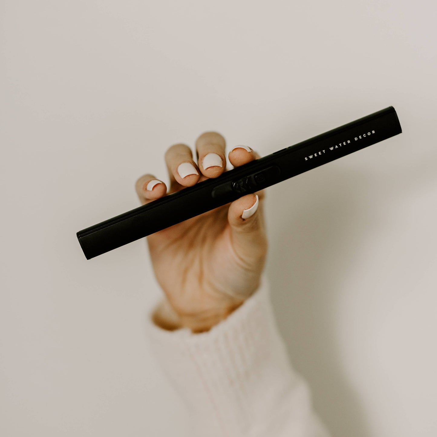 Hand holding a black pen with 'Sweet Water Design' branding against a neutral background