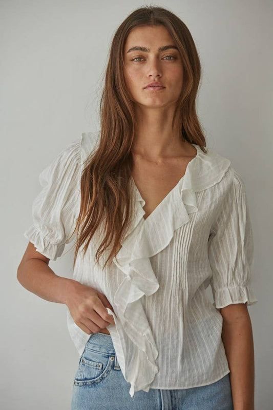 Woman wearing a white blouse with ruffled details against a plain background