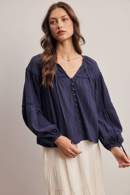Woman wearing a navy blue blouse with long sleeves and a neutral background