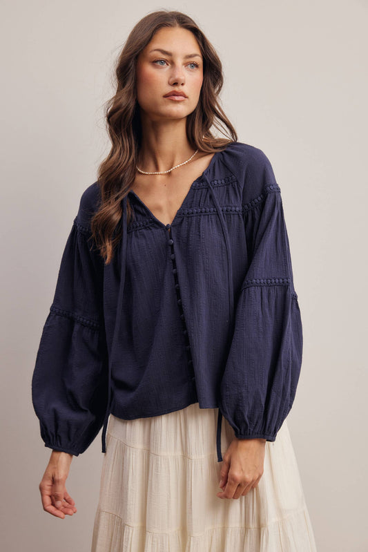 Woman wearing a navy blue blouse with long sleeves and a white skirt on a neutral background