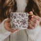 Person holding a floral-patterned mug with a gold handle