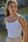Woman wearing a white tank top and beige pants outdoors
