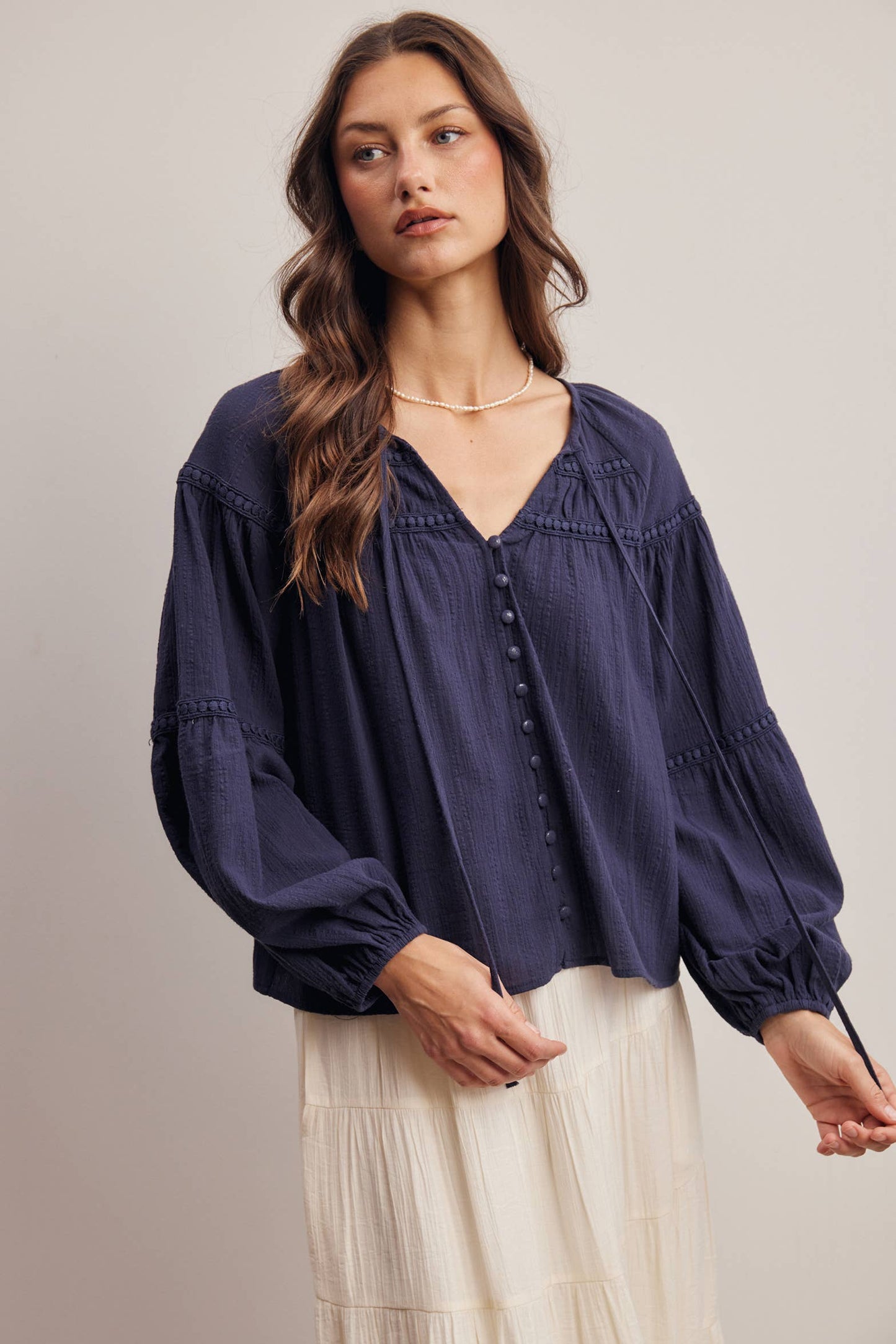Woman wearing a navy blue blouse with long sleeves and a neutral background
