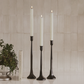 Three tall black candle holders with white candles against a neutral background