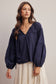 Woman wearing a navy blue blouse with long sleeves and a white skirt on a neutral background