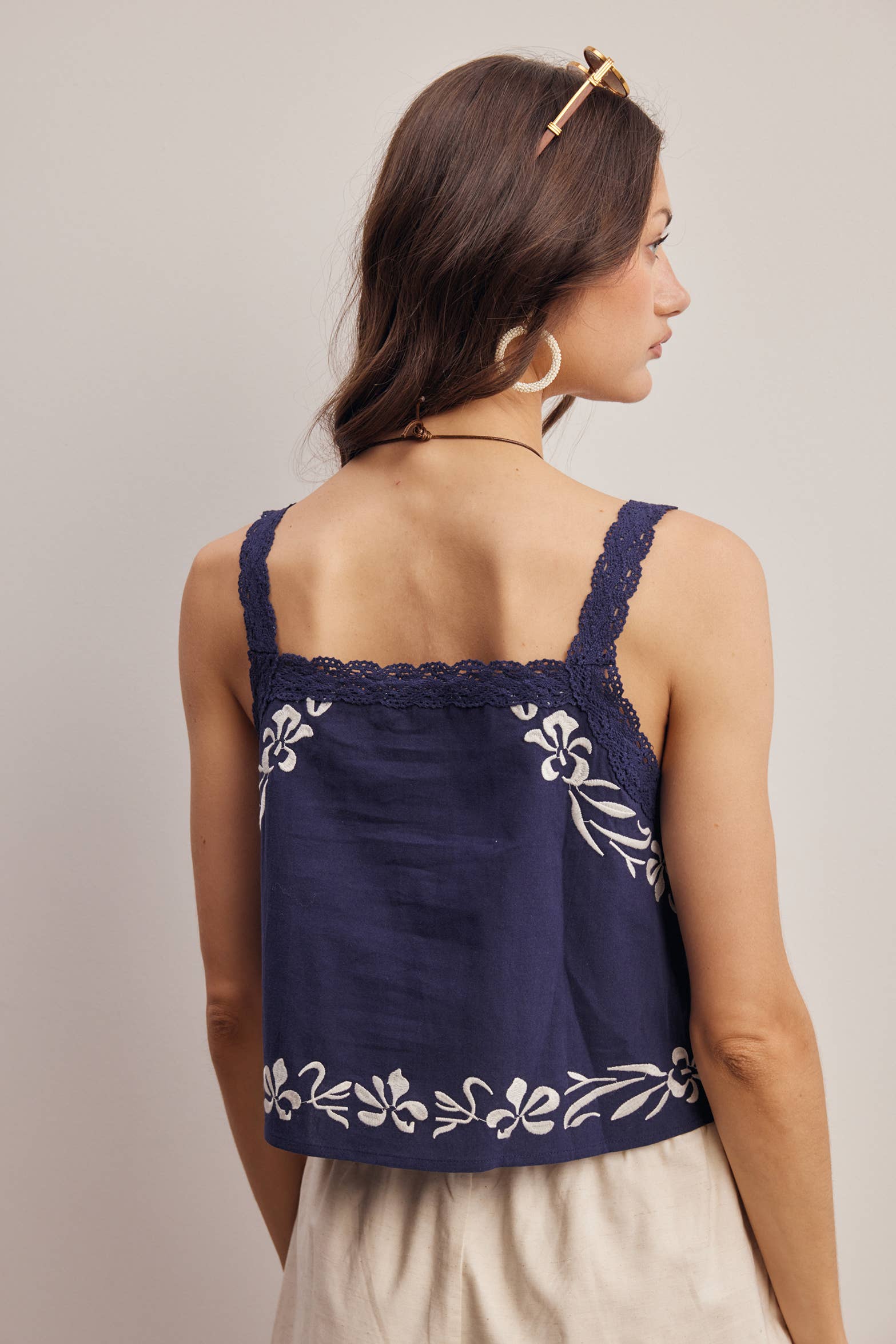Woman wearing a navy blue top with white floral embroidery on a plain background