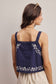 Woman wearing a navy blue top with white floral embroidery on a plain background