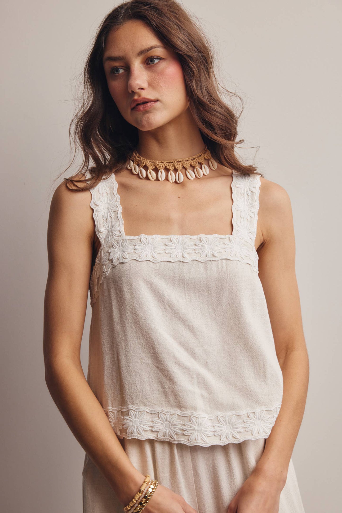 Woman wearing a beige sleeveless top with lace details against a plain background