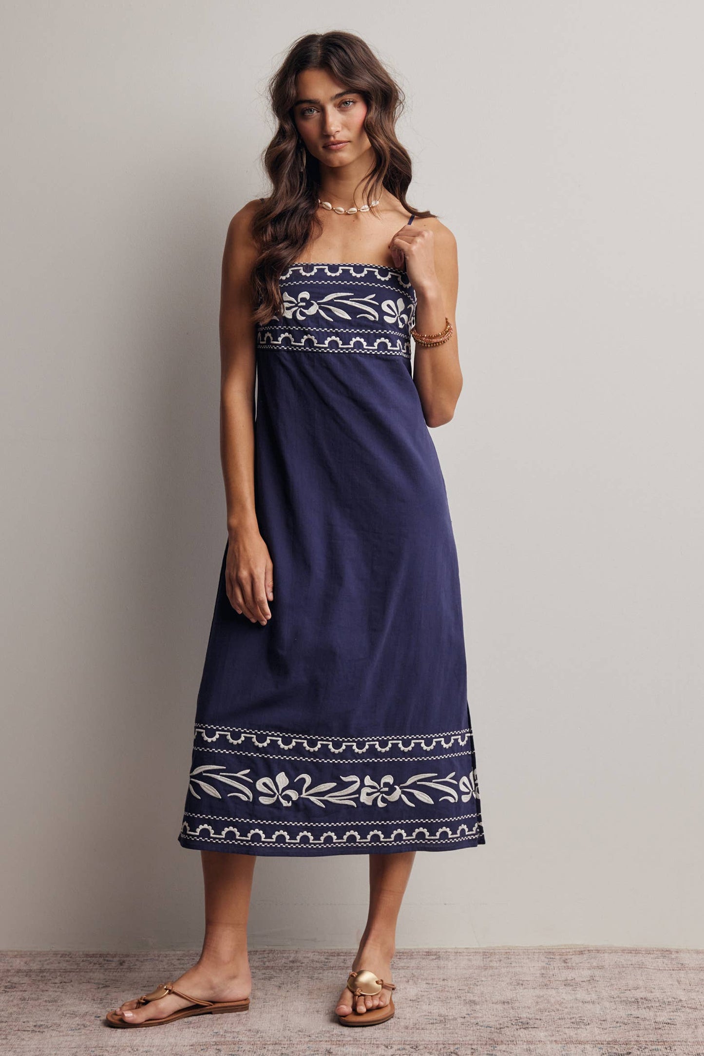 Woman wearing a blue dress with white embroidery against a plain background