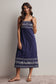 Woman wearing a blue dress with white embroidery against a plain background
