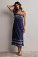 Woman wearing a navy blue dress with white patterns against a plain background