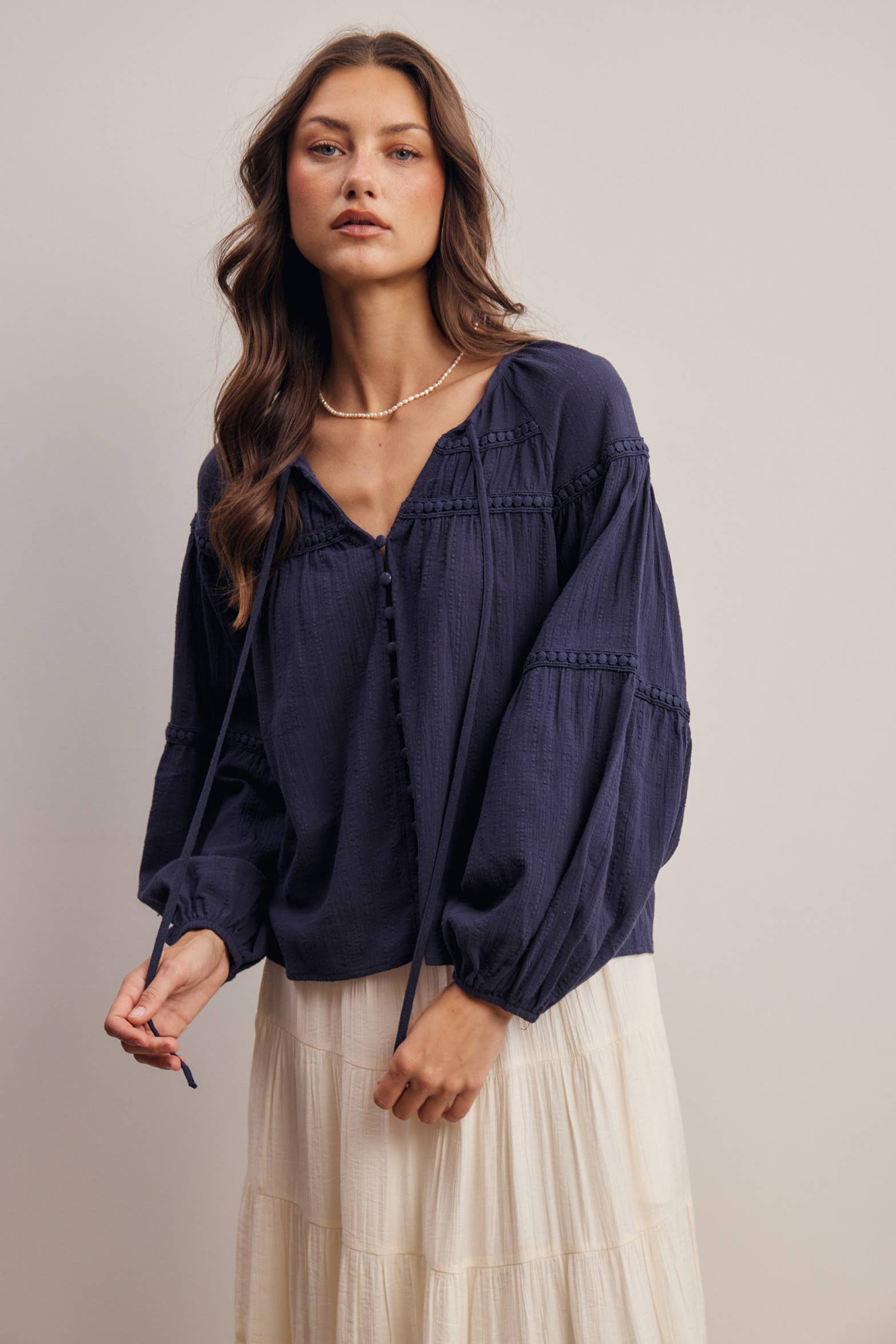 Woman wearing a navy blue blouse with long sleeves and a cream skirt on a plain background