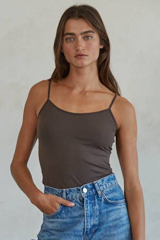 Woman wearing a brown tank top and blue jeans against a plain background