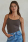 Woman wearing a brown tank top and blue jeans against a plain background
