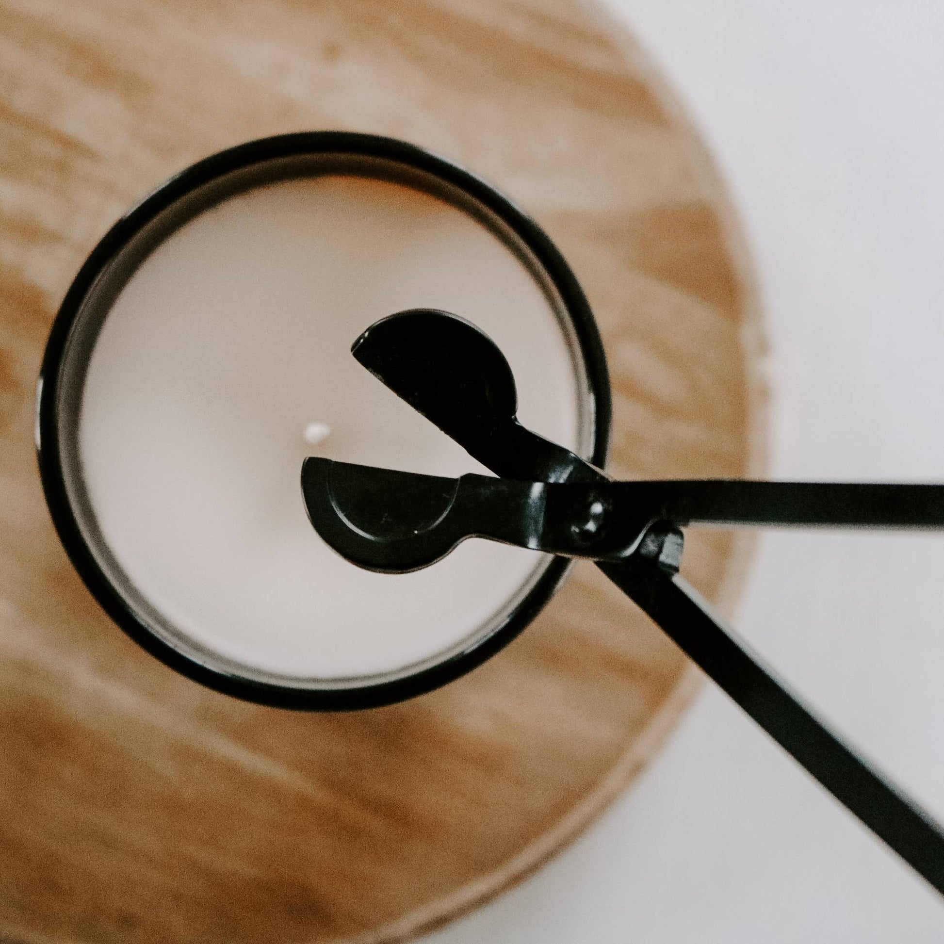 Close-up of a spoon stirring a cup of coffee on a wooden coaster.