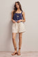 Woman wearing a navy top and beige shorts against a plain background
