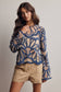 Woman wearing a blue and beige patterned top with beige shorts on a plain background