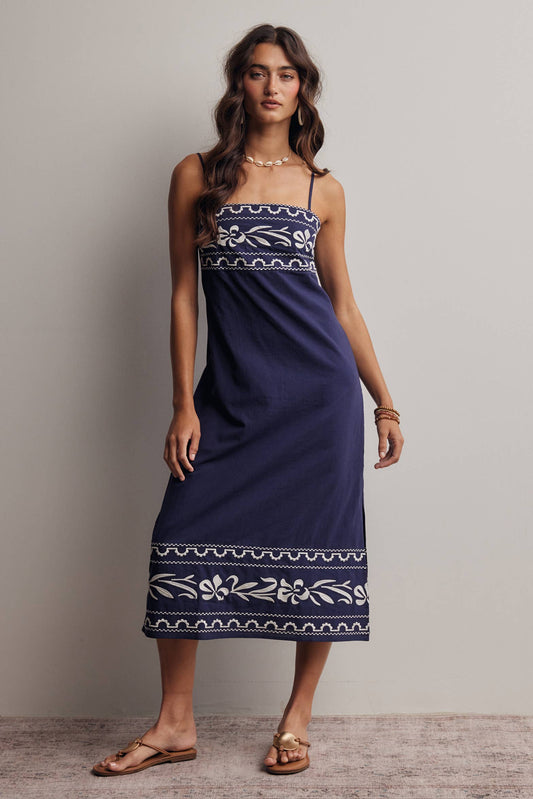 Woman wearing a navy blue dress with white patterns against a plain background
