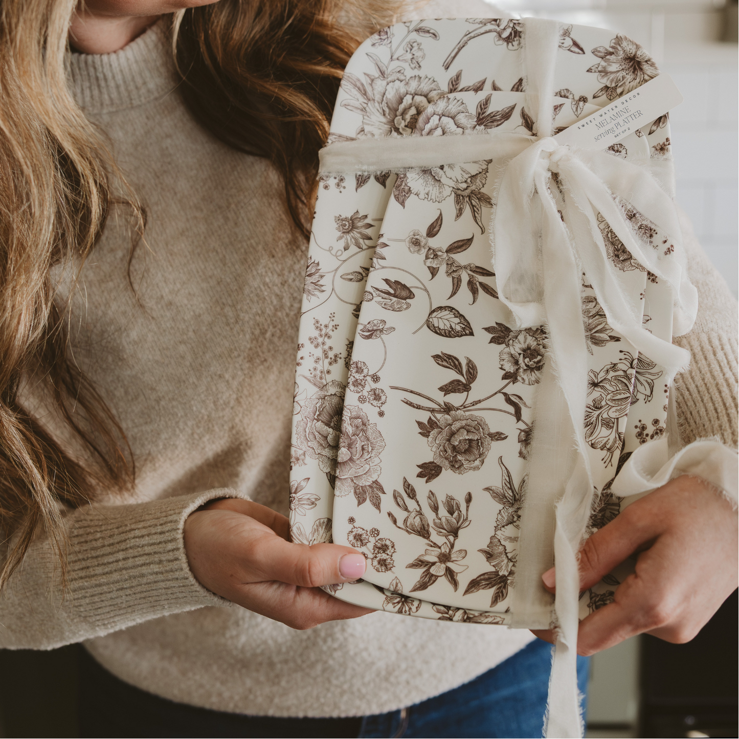 Woman holding a floral-patterned gift box in a kitchen setting