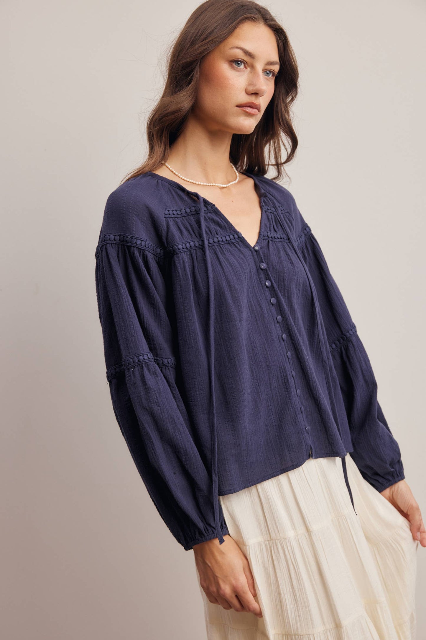 Woman wearing a navy blue blouse with long sleeves and a V-neckline on a plain background