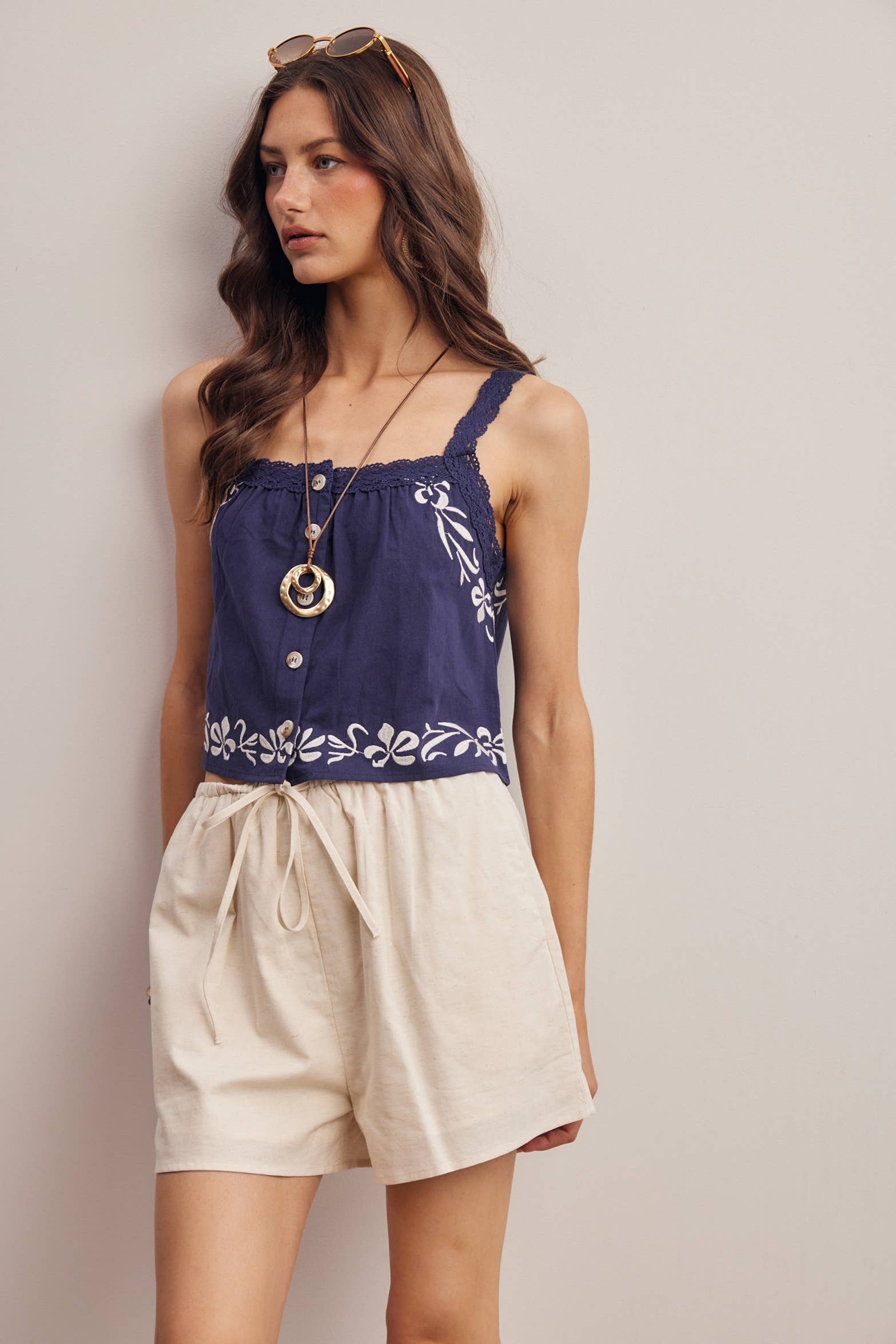 Woman wearing a blue embroidered top and beige shorts against a plain background