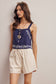 Woman wearing a blue embroidered top and beige shorts against a plain background